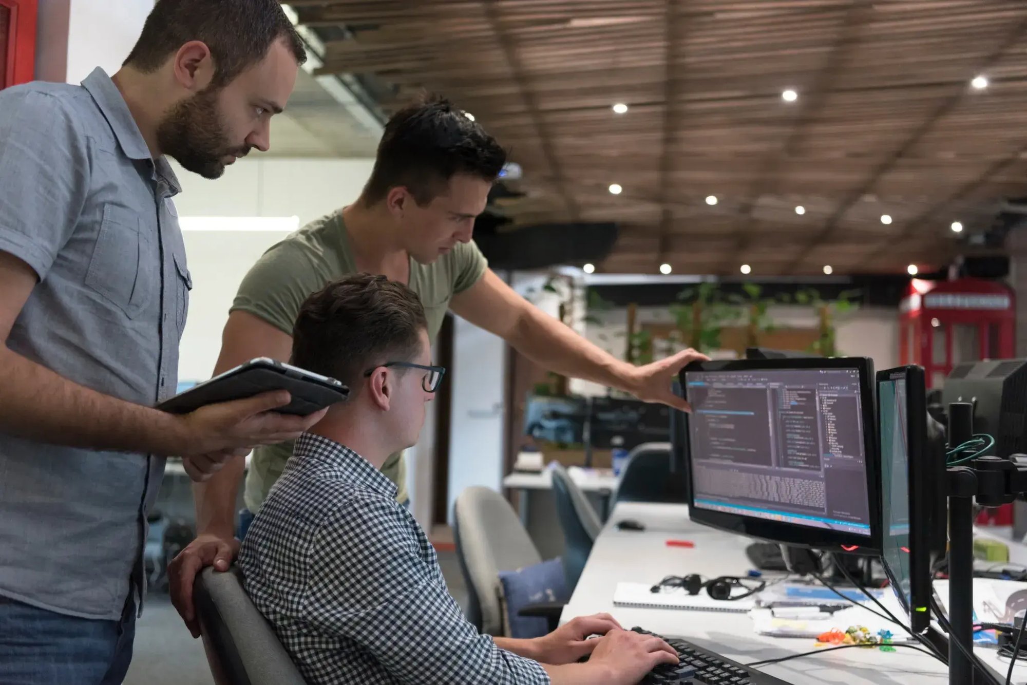 Equipo de desarrolladores colaborando frente a una computadora en una oficina moderna Equipo de desarrolladores colaborando frente a una computadora en una oficina moderna