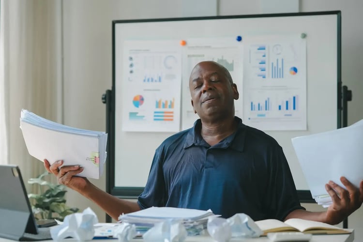 man at his desk, engaged with papers and a laptop, exemplifying a busy work environment.