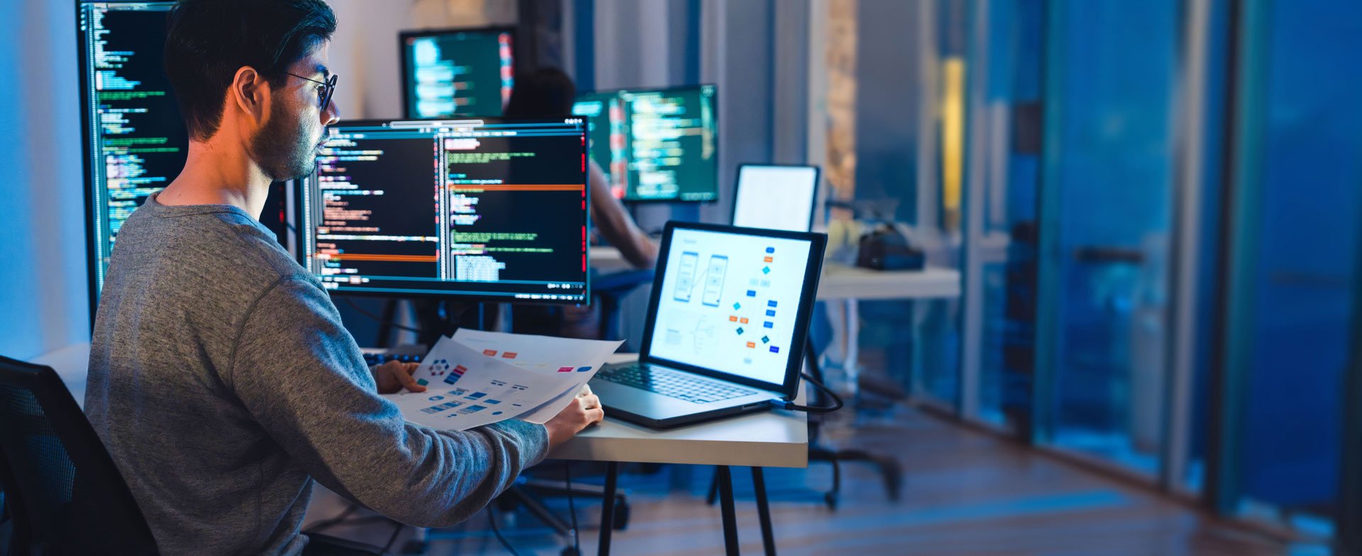 A man working at a desk with two computers, illustrating nearshore software development A man working at a desk with two computers, illustrating nearshore software development