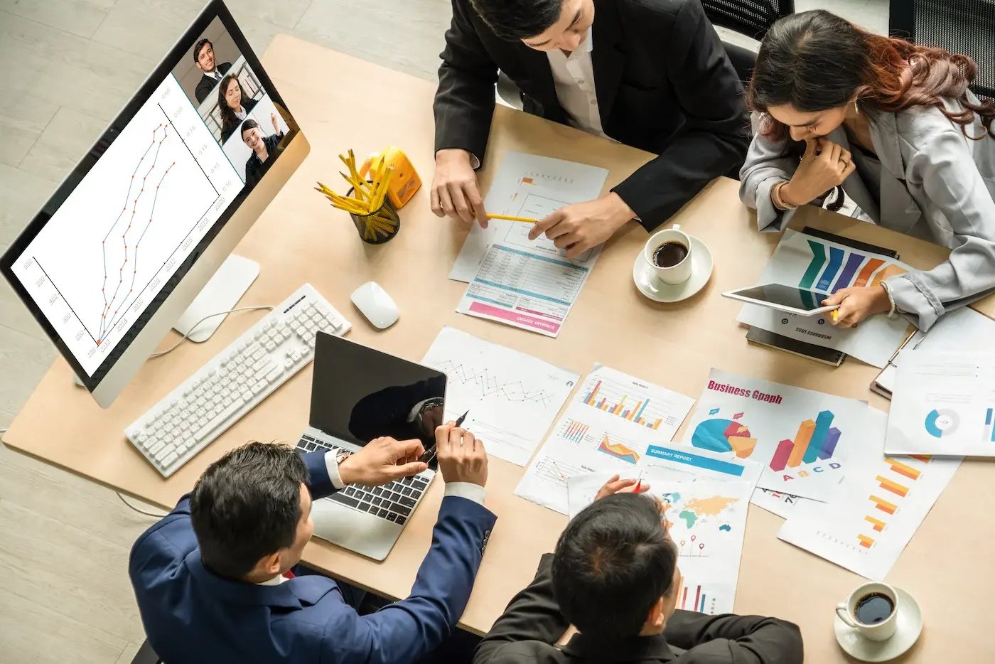 a group of professionals on a cluttered worktable with several devices, graphs and charts on documents