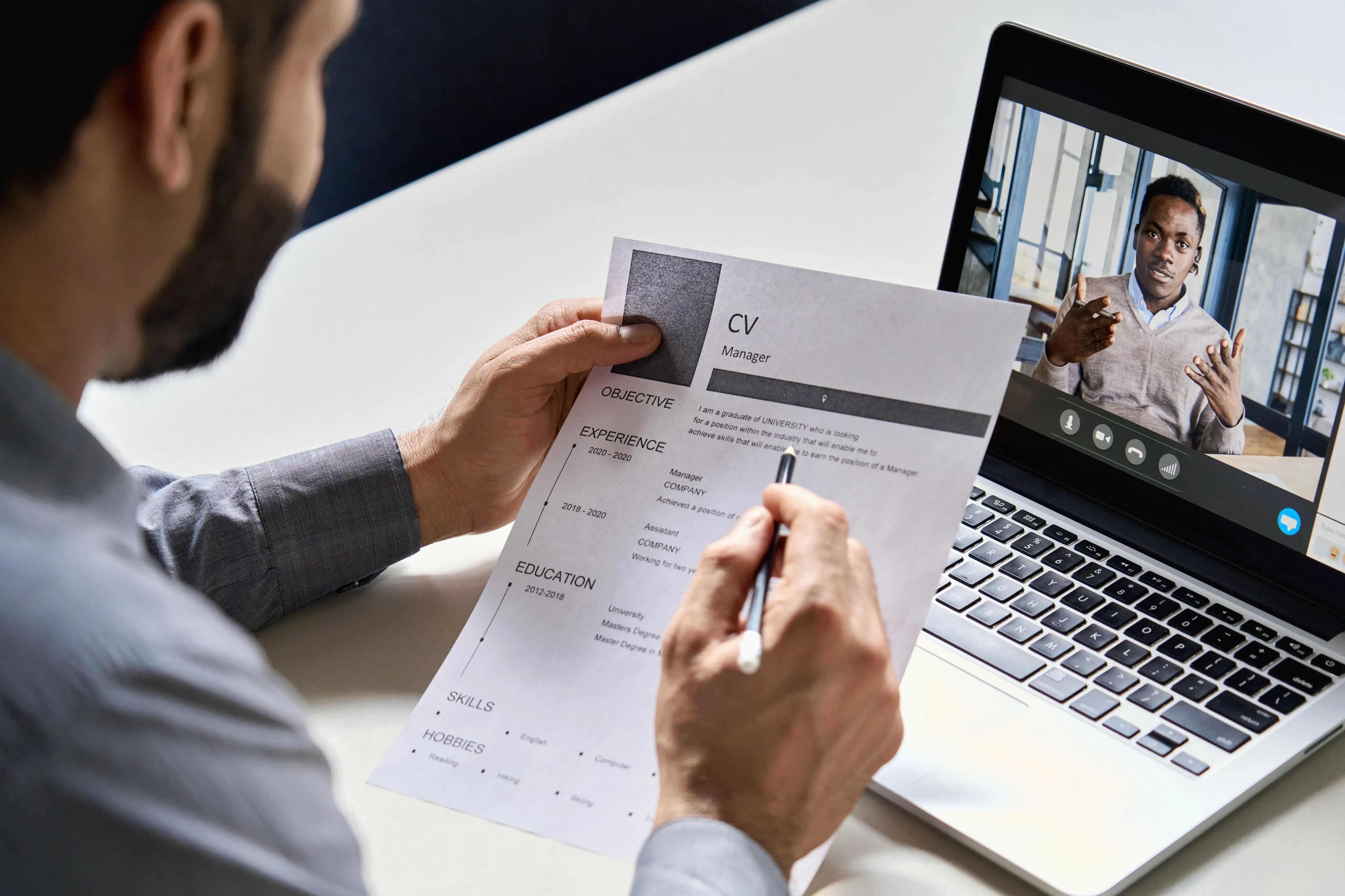 A person holding a resume is participating in a video interview on a laptop