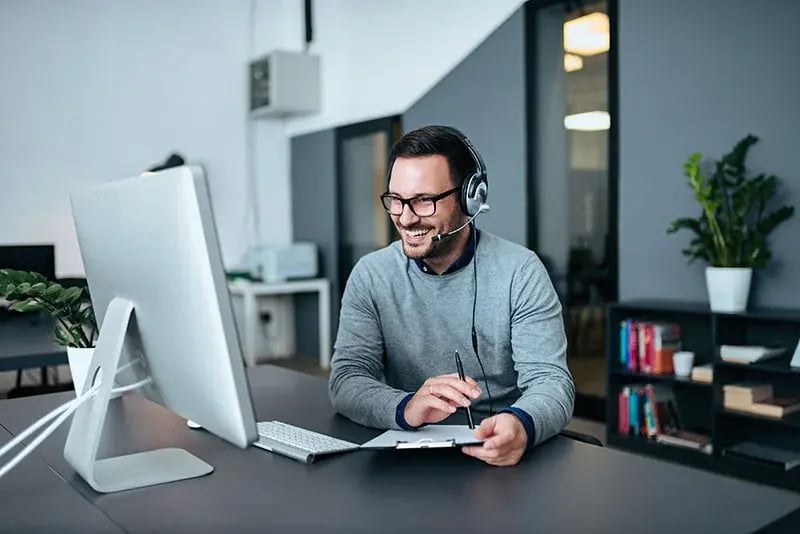 Man smiling while looking at a desktop computer with headphones on