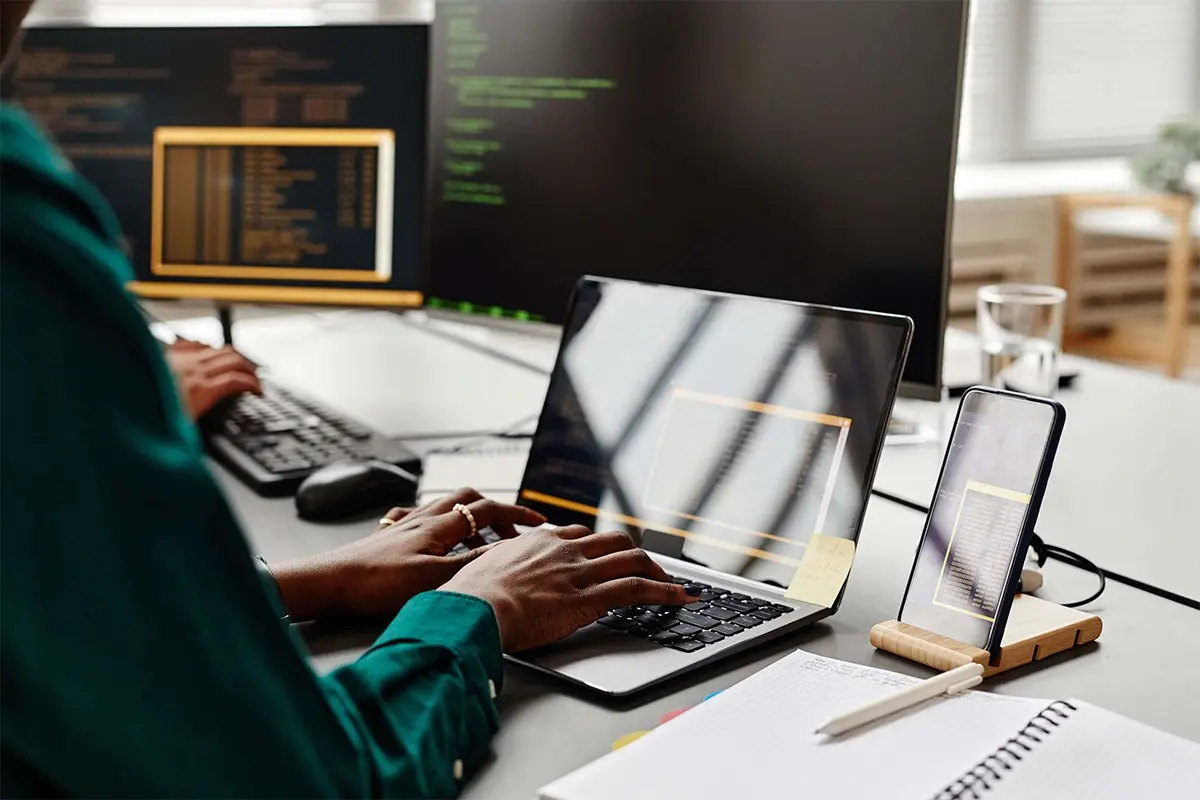 a person on a laptop, with a phone and a computer nearby